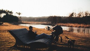 A person sitting on a bench with a dog nearby, a body of water in the background, and trees around. - Resort Stara Wieś (Patnów)