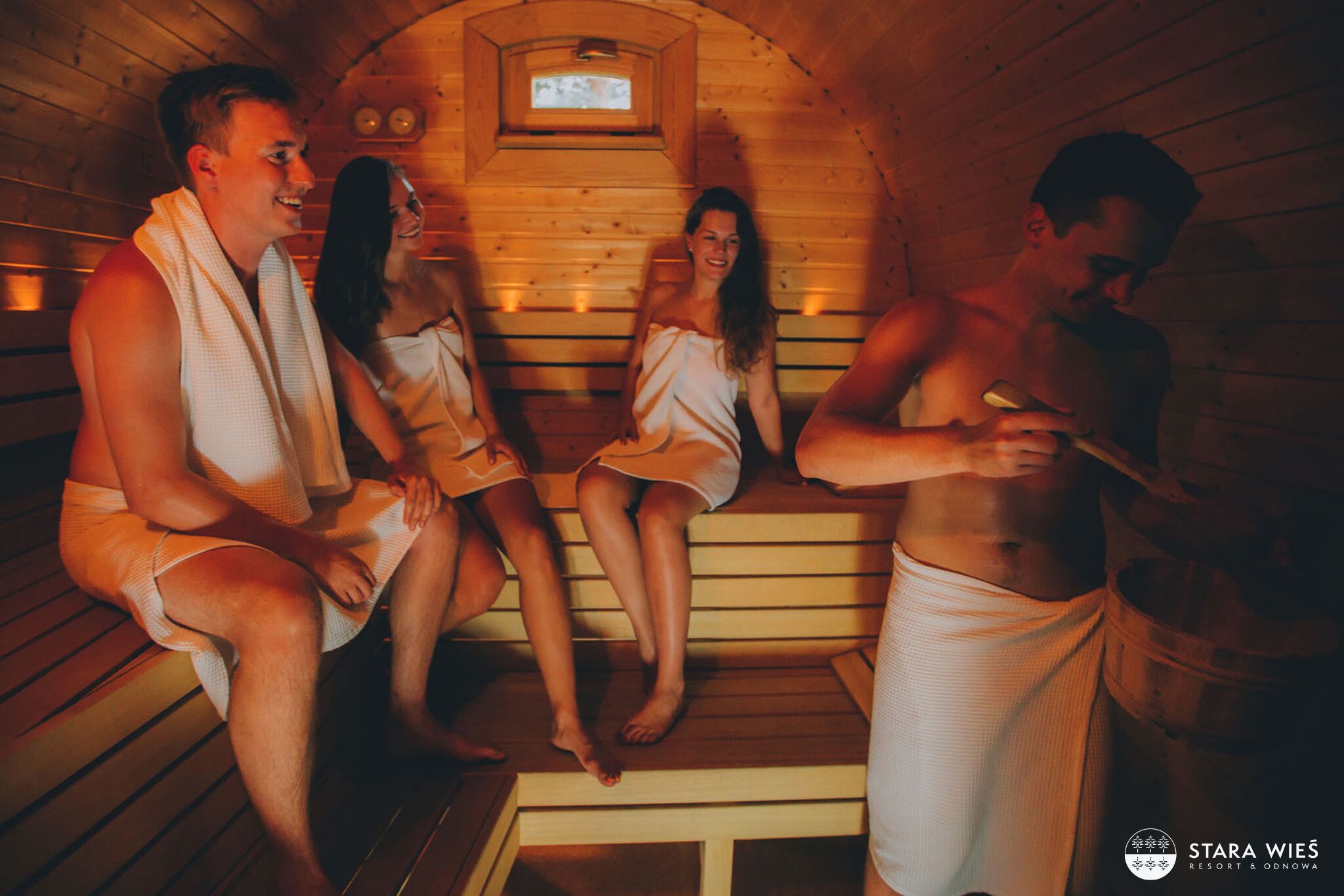 Una sauna con pareti e panche in legno, una piccola finestra e una persona avvolta in un asciugamano.