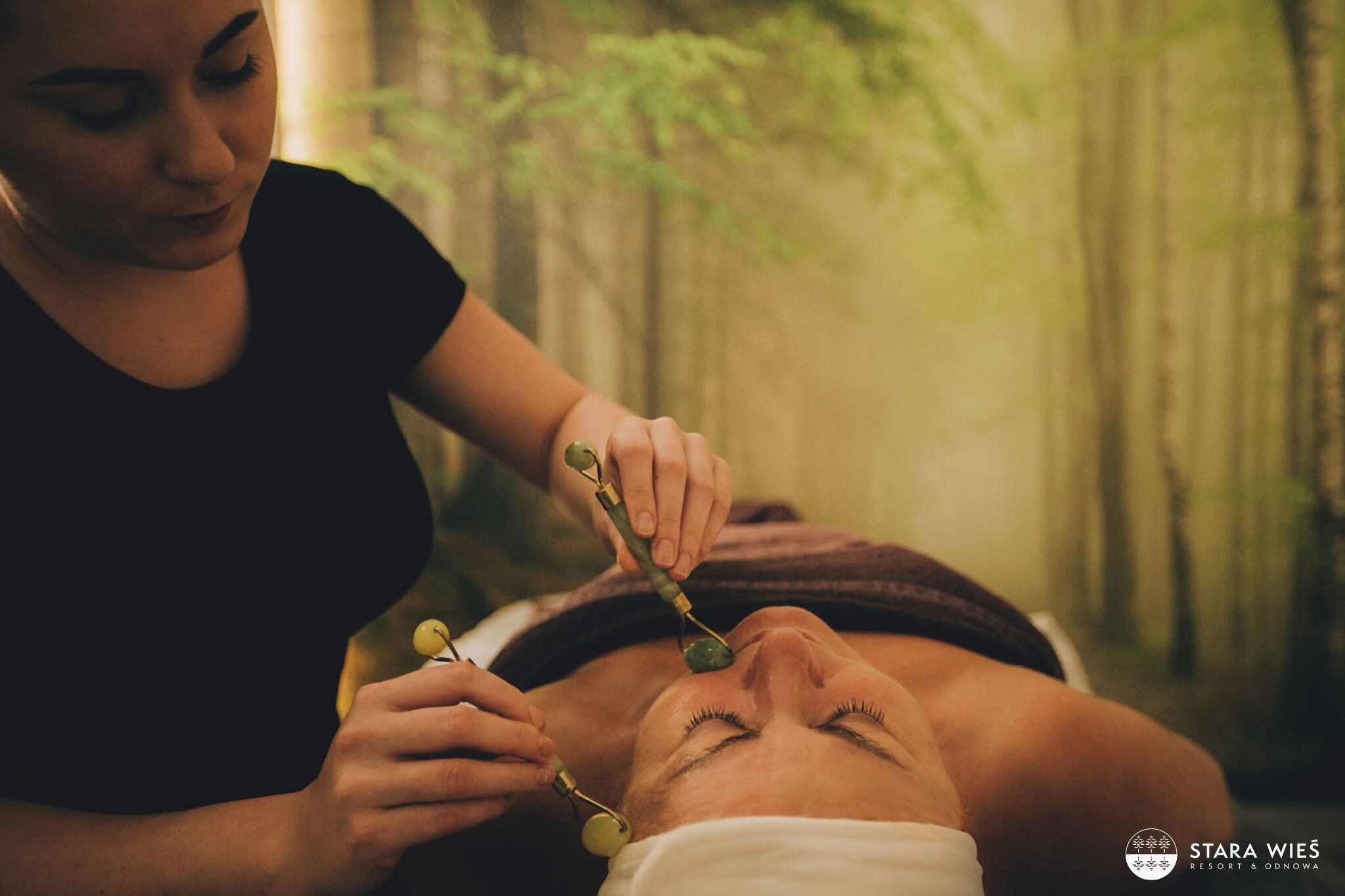 A person receiving a facial treatment with jade rollers.
