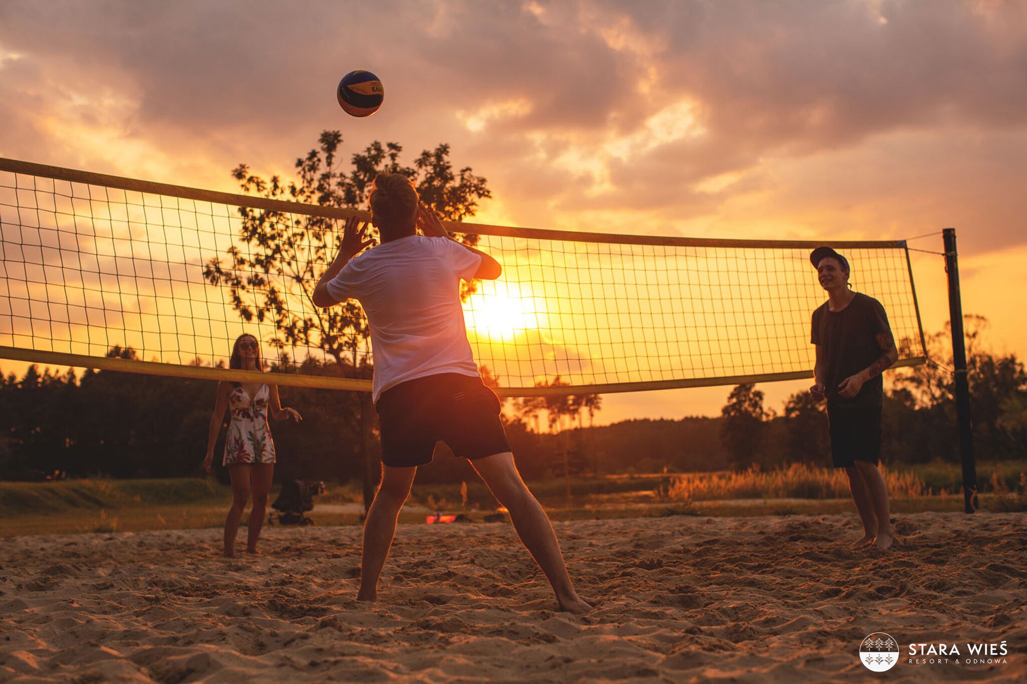Partido de voleibol de playa al atardecer con red y jugadores.