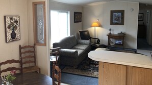 Ett mysigt vardagsrum med ett matbord i trä, en mönstrad fåtölj, en lampa och ett litet sidobord med en dekorativ prydnad.
