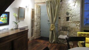 Une pièce rustique avec un mur en pierre, des poutres en bois au plafond, un rideau, une petite table avec une chaise et un téléviseur fixé au mur.