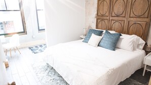 A bedroom with a large bed, a wooden headboard, a white bedside table, and a small nightstand. - Luxury apartment with a private rooftop deck located in the heart of downtown JC (Johnson City)