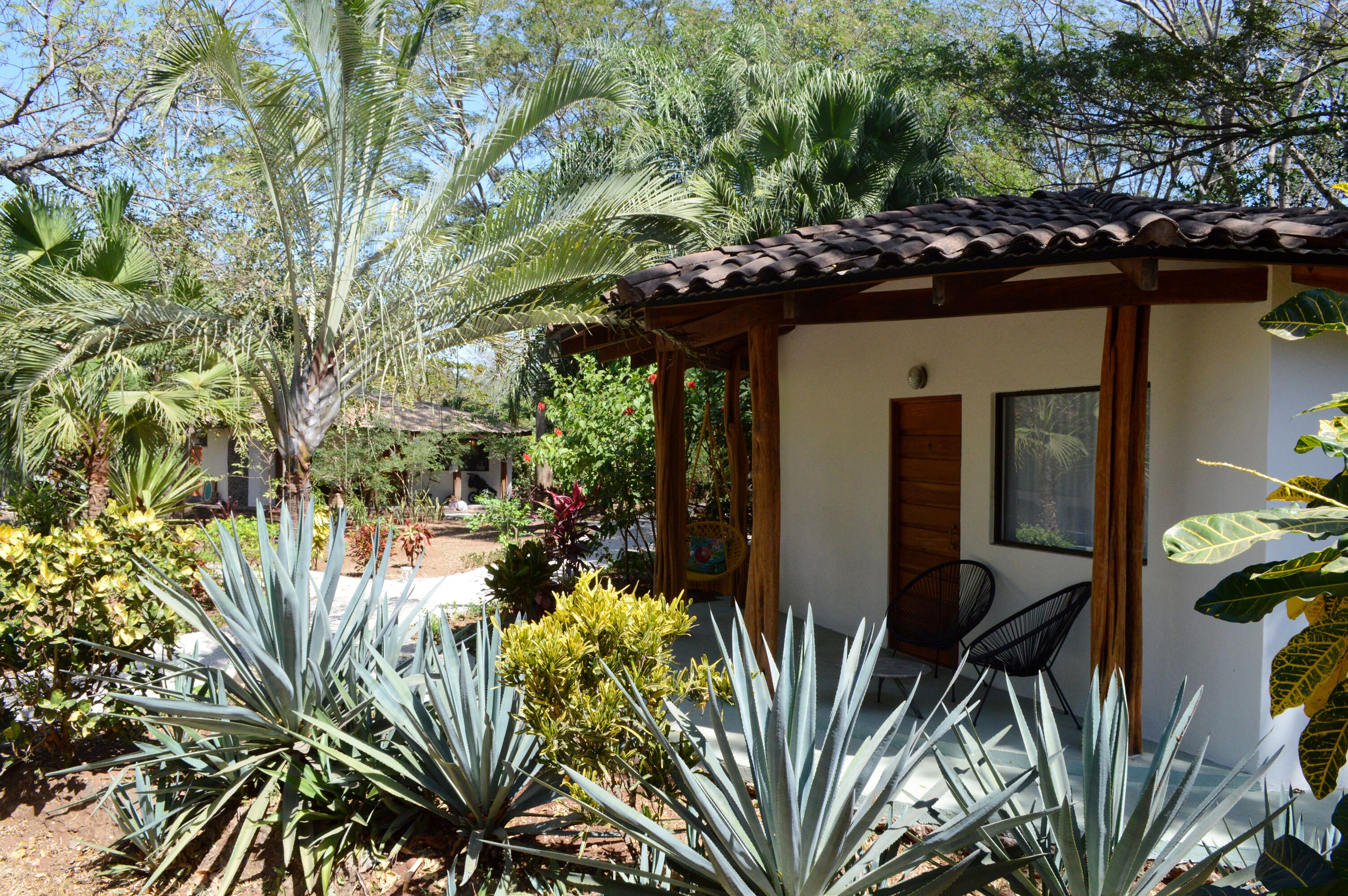 A small house with a tiled roof, surrounded by various plants and trees.