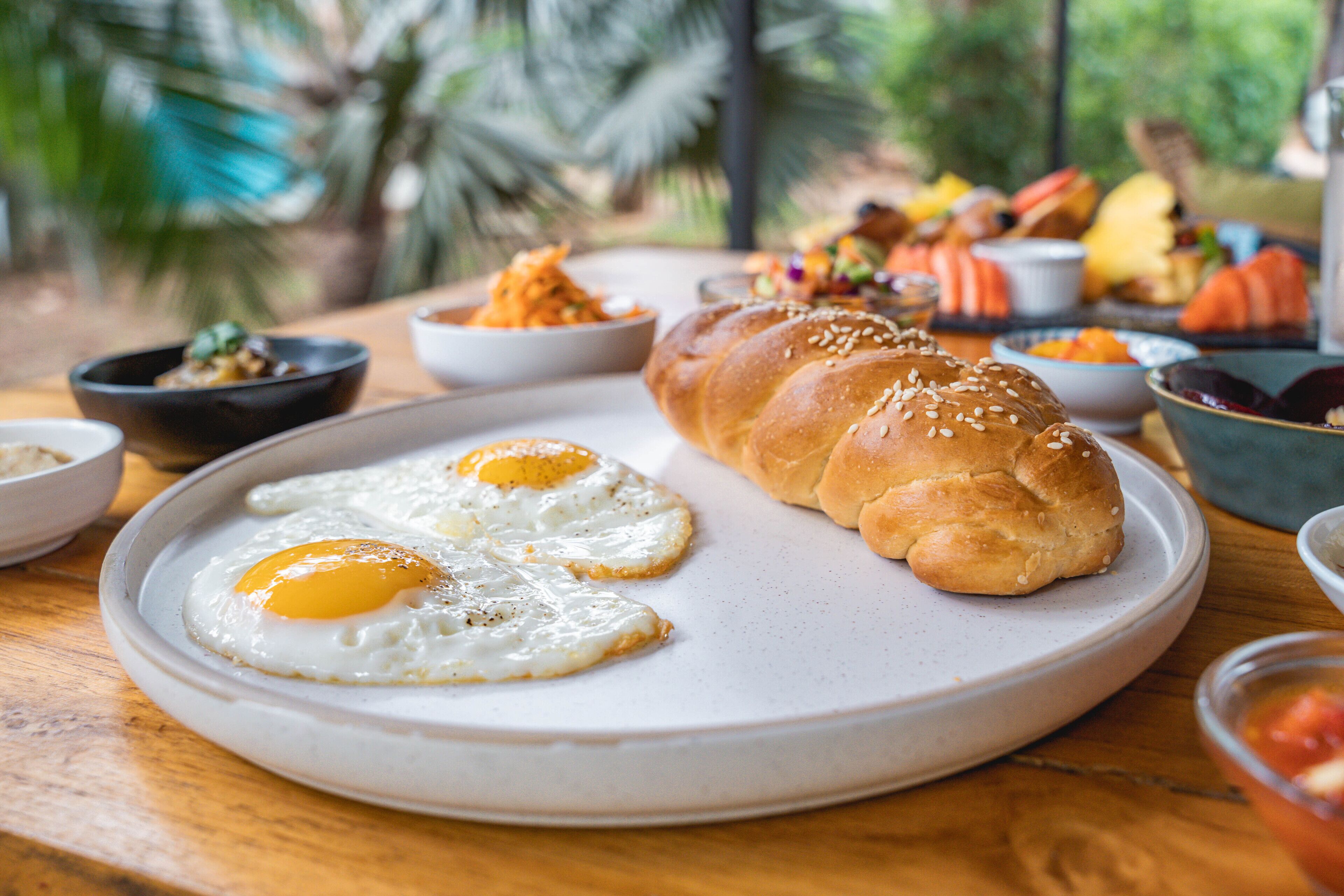 Un desayuno con huevos, pan y diferentes acompañamientos sobre una mesa de madera.