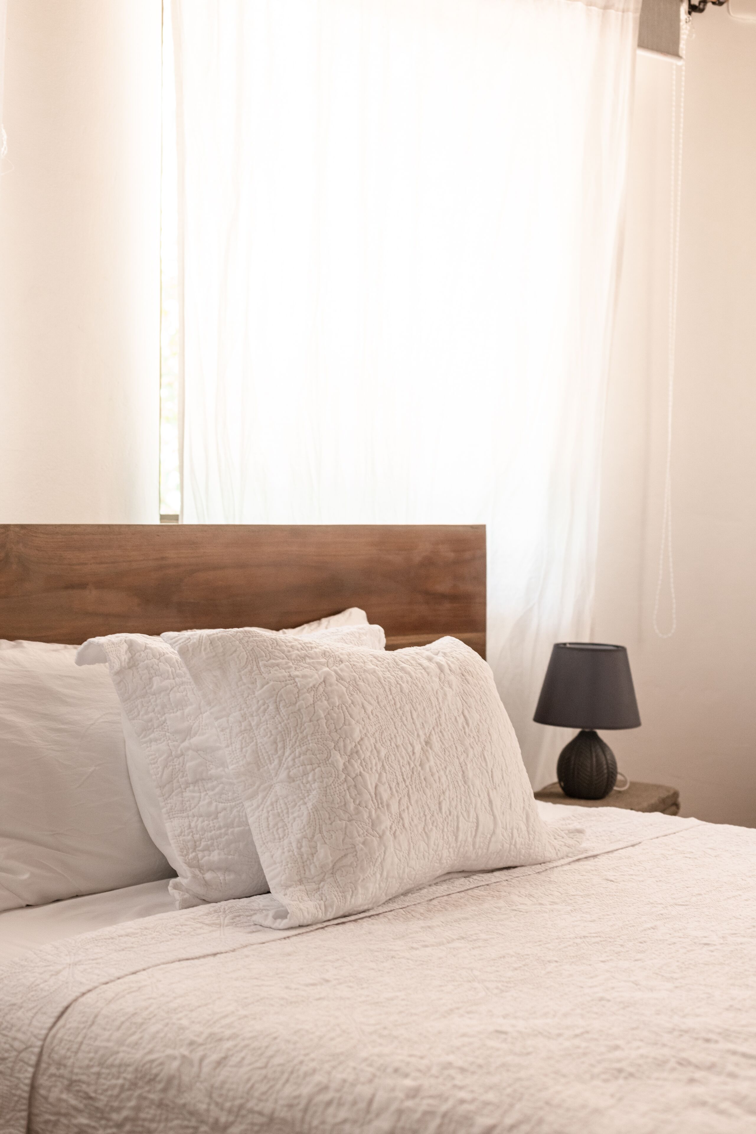 A neatly made bed with white linens and a wooden headboard.