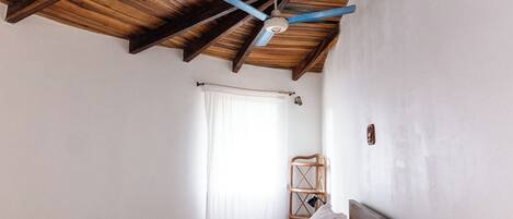A bedroom with a wooden ceiling, a bed with white bedding, a small round table, and a woven rug.