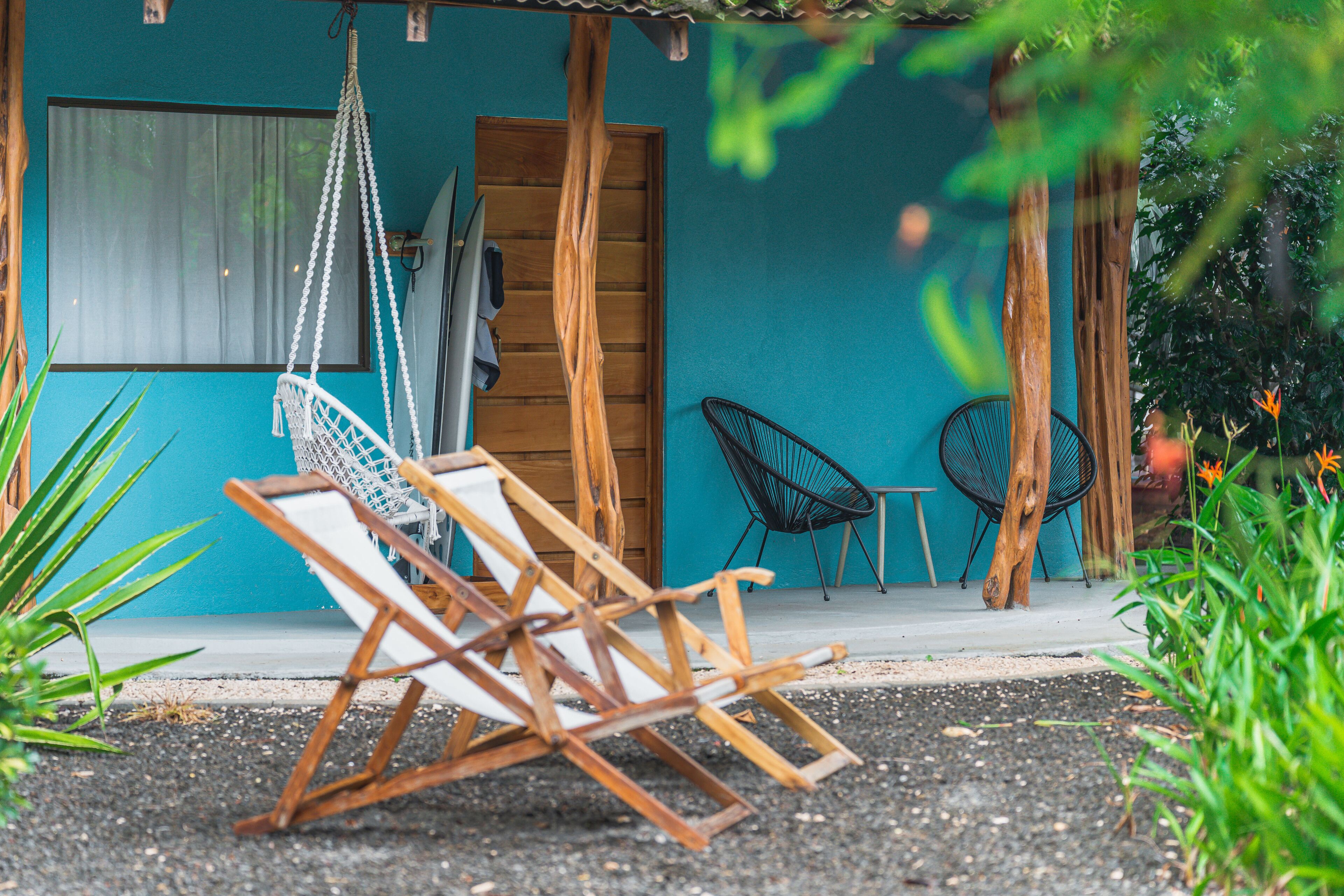 A wooden chair and a hammock outside a building with a blue exterior.