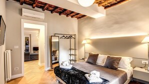 Ein modernes Schlafzimmer mit Holzboden, einem Bett mit schwarz-weißer Bettdecke, Nachttischlampen und einem Spiegel mit Kleiderstange.