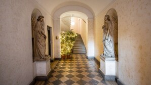 Ein Korridor mit Statuen an beiden Seiten, einem Schachbrettboden und einer Treppe im Hintergrund.