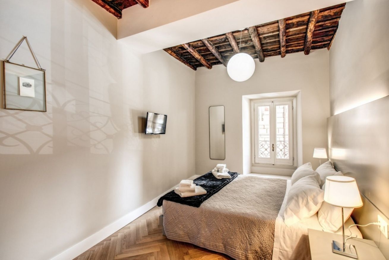 A bedroom with a bed, bedside table, lamp, and a window with a view.