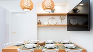 Een eetruimte met een houten tafel voor zes personen, witte stoelen en hangende rieten lampen.