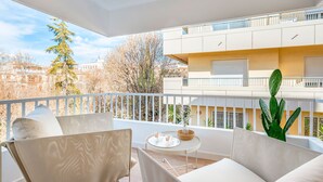 Een balkon met uitzicht op gebouwen, een cactus en een tafel met een mand en glazen.