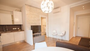 Ein modernes Wohnzimmer mit Fernseher, weißen Sesseln und einem Esstisch.