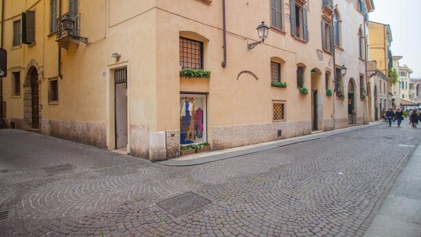 Eine Kopfsteinpflasterstraße mit einem Gebäude, das einen Laden, Rundbogenfenster und einen mit Grünpflanzen bepflanzten Balkon zeigt.