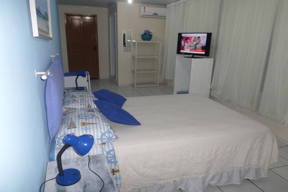 Un dormitorio con cama, escritorio con ordenador, televisor y puerta.