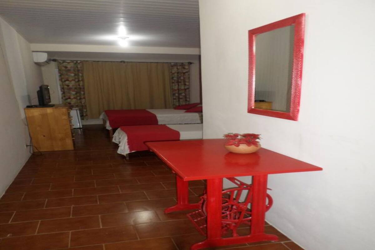 Una habitación pequeña con una mesa roja, una cama con ropa de cama roja y un espejo en la pared.