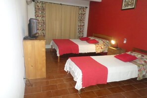 A room with two beds, each with a red and white bedspread, a wooden dresser, a television, and a red wall. - OYO Hotel Rainha (Itapoa)