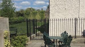 Un patio exterior con mesa y sillas, una cerca de metal negro y una pared blanca.