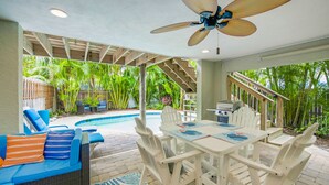 Un patio exterior con piscina, mesa de comedor y ventilador de techo.