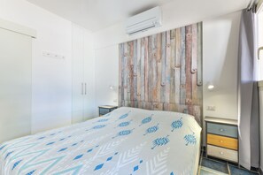 Hotellihuone, jossa on sänky, lipasto, ilmastointilaite ja seinä, jossa on puupaneelista tehty koristeellinen kuvio.