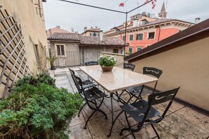 An outdoor patio with a table and chairs, surrounded by buildings. - Romeo Terrace (Verona)