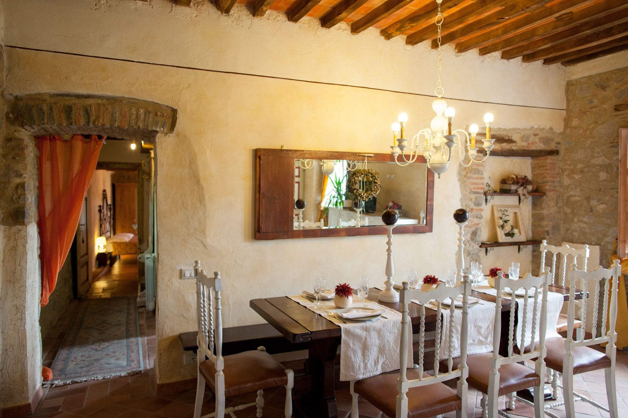 Comedor con mesa de madera dispuesta para cuatro personas, sillas blancas y una lámpara de araña.