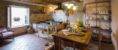 Una cocina rústica con una mesa de comedor dispuesta para una comida, un perro acostado en el suelo y una ventana con flores afuera.