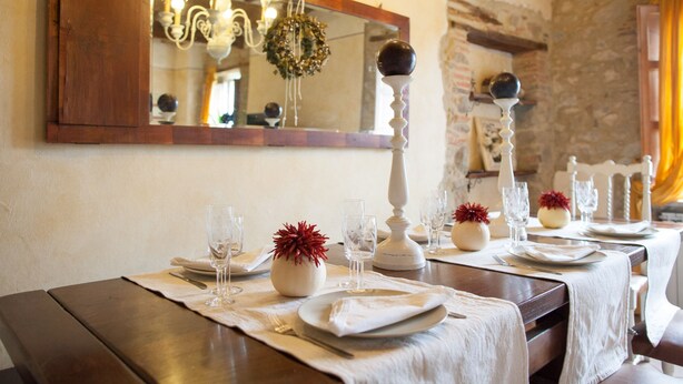 A dining table set with white tablecloths, glassware, and red decorative elements. - Stone house with 4 double bedrooms and kitchen with fireplace (Boveglio)