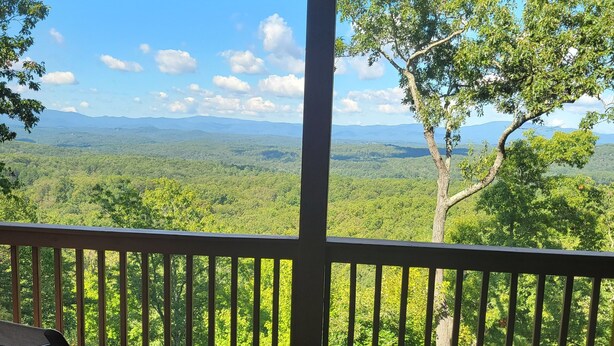 Une terrasse en bois avec une table et des chaises, offrant une vue sur un paysage boisé et des montagnes lointaines.