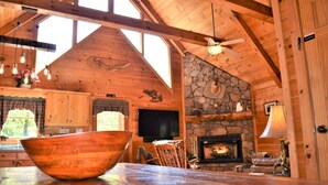 L’intérieur d’un chalet rustique, avec une cheminée en pierre, des poutres en bois au plafond et une grande table en bois sur laquelle se trouve un saladier.