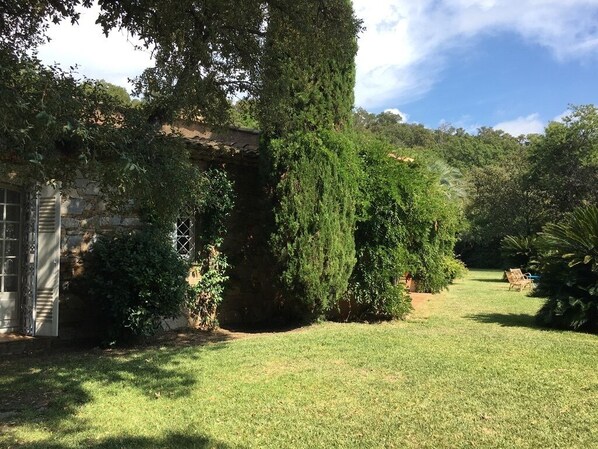 A well-maintained garden with a stone building, lush greenery, and a clear sky.