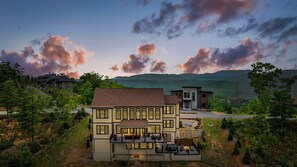 A two-story house with a balcony and a patio area, surrounded by trees and a mountainous landscape in the background. - Summit 86 - 6,000 sq ft Luxury Cabin w/Indoor Pool, Golf Simulator, Fire Pit! (Sevierville)