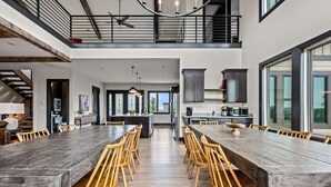 Un comedor amplio con una larga mesa de madera y sillas, una cocina con electrodomésticos modernos, y ventanas grandes que dejan entrar luz natural.