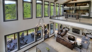 Amplio espacio habitable de varios niveles con ventanas grandes, un candelabro y una chimenea.