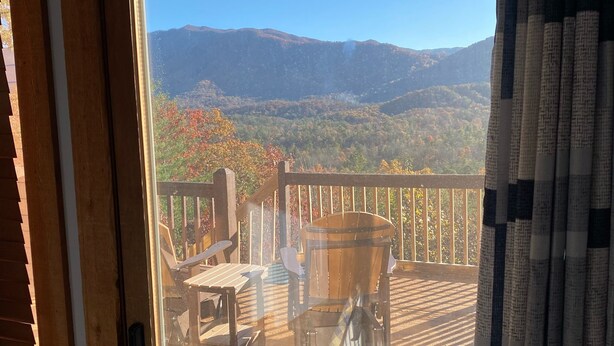 Una terraza de madera con muebles de exterior, vista a las montañas y cielo despejado.