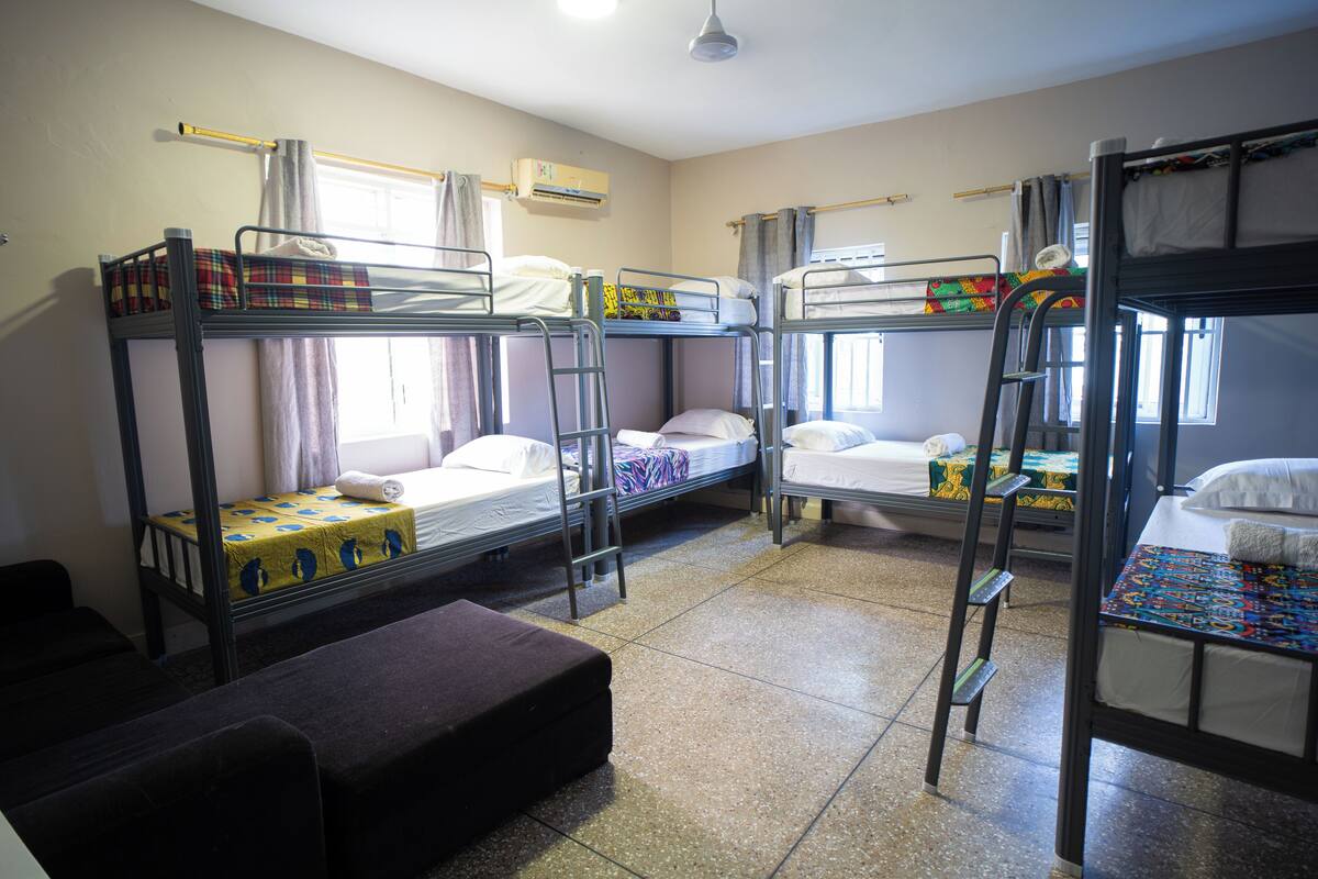 Quarto em dormitório com beliches, um pequeno sofá e uma janela com cortinas.