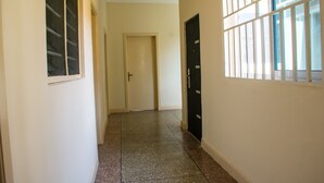 A hallway with a door at the end, a window with bars, and a tiled floor. - Brannic Lodge - Hostel (Accra)