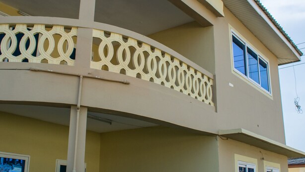 A two-story building with a balcony, potted plants, and a clear sky. - Brannic Lodge - Hostel (Accra)