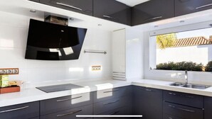 Une cuisine moderne avec des meubles de couleur sombre, un pare-feu noir et une fenêtre donnant sur un immeuble et de la verdure.
