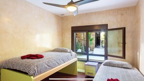 Une chambre avec deux lits, un ventilateur de plafond et une vue sur l’extérieur.
