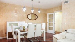 Un coin repas avec une table et des chaises blanches, un luminaire suspendu et une porte donnant sur une autre pièce.