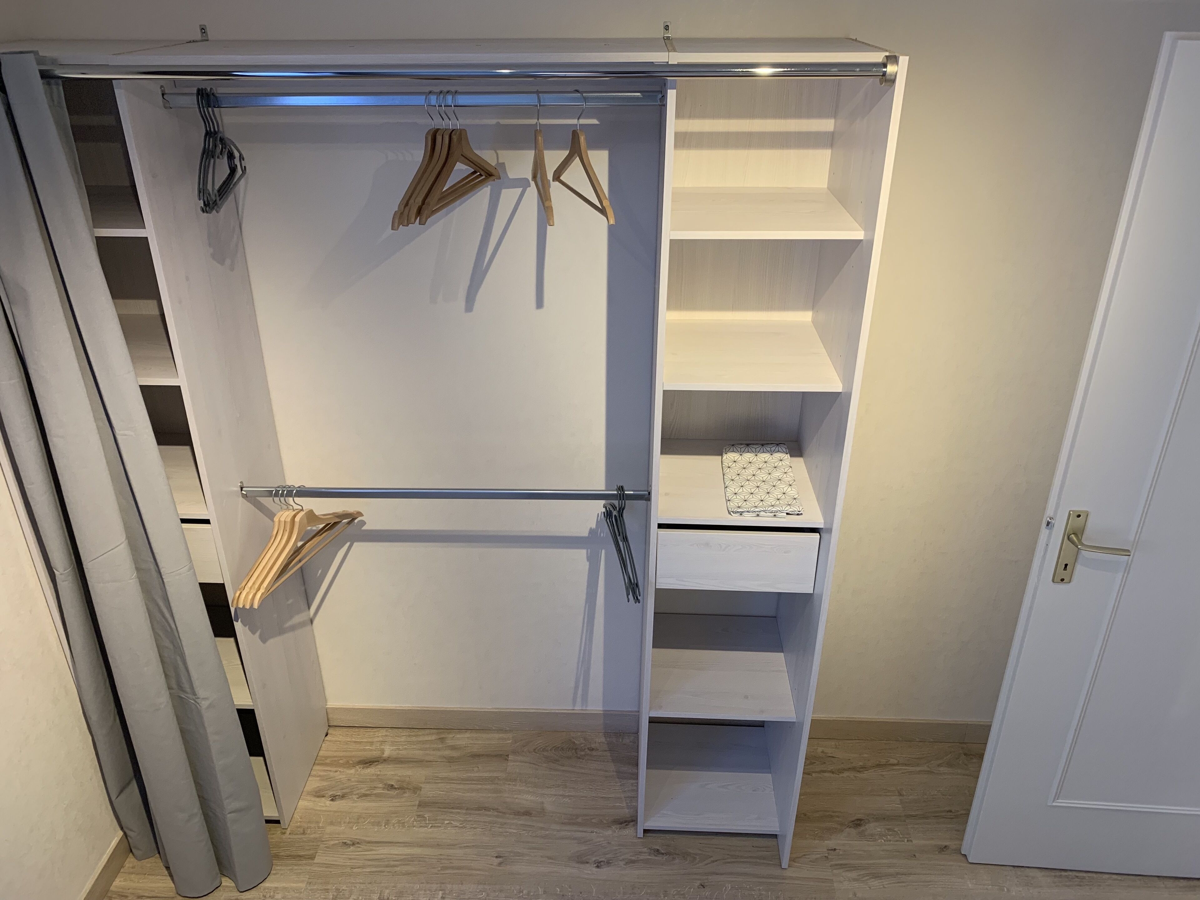 Ein begehbarer Kleiderschrank mit offenen Regalen, einer Kleiderstange und einer Schiebetür.