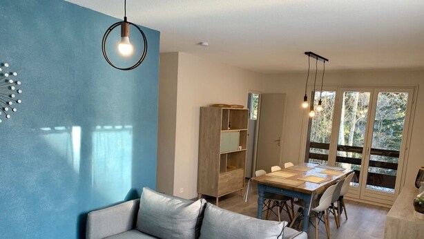 Un salon moderne avec un canapé gris, une table à manger en bois et un mur d’accent bleu.