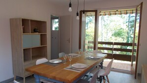 Un coin repas avec une table en bois dressée pour quatre personnes, entourée de chaises, avec une bibliothèque et une fenêtre donnant sur un paysage verdoyant.