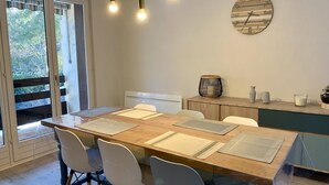 Un espace repas avec une table en bois, des chaises blanches et des luminaires suspendus.