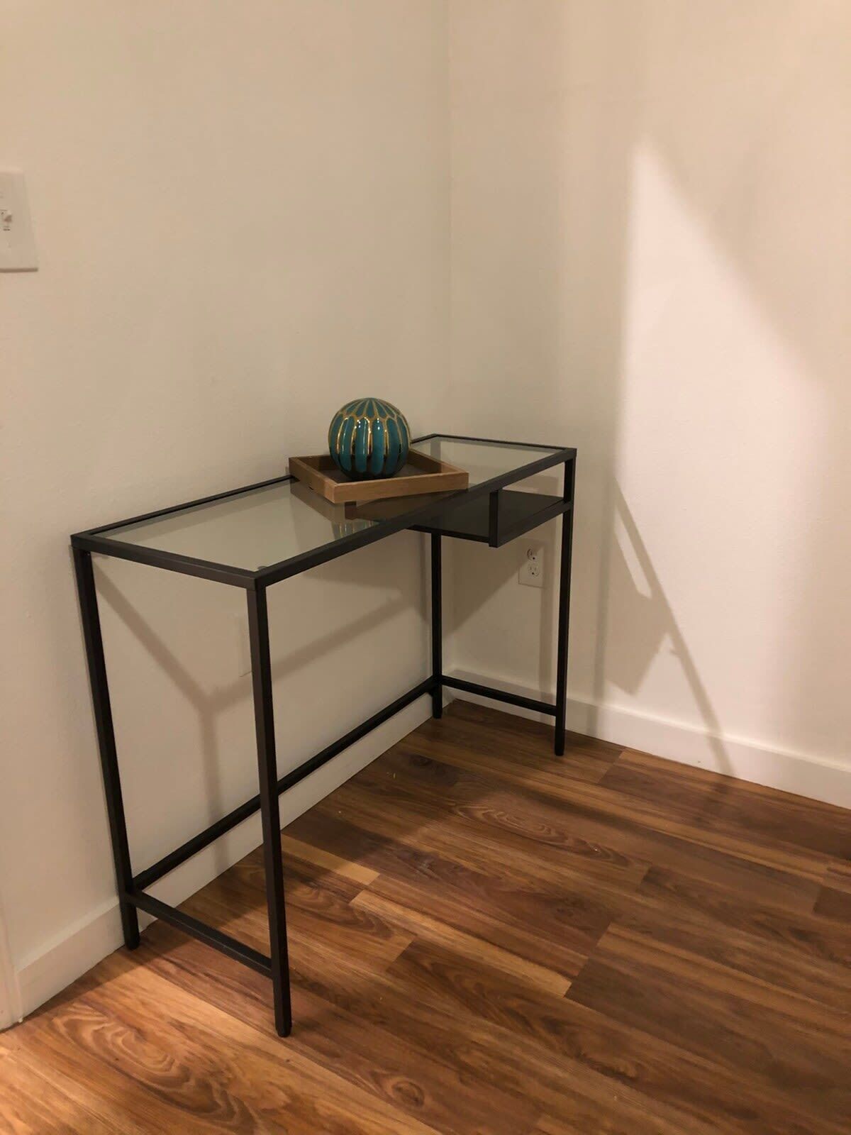 A corner desk with a glass top and black metal frame, a wooden tray, and a decorative globe.