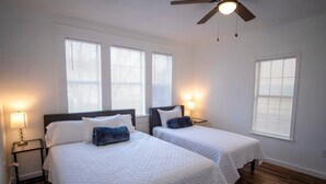 A bedroom with two beds, a ceiling fan, and a nightstand with a lamp.