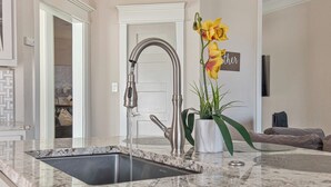 Una cocina con un lavamanos de acero inoxidable, un jarrón blanco con flores y una puerta al fondo.