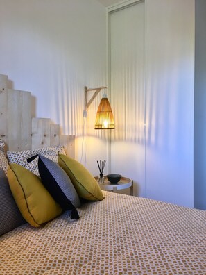 Et soveværelse med en seng, puder, et sengebord med lampe og et vindue med persienner.